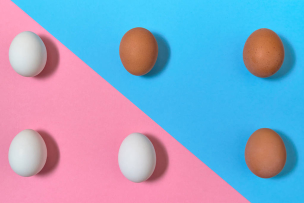 weiße und braune Eier auf blauem und rosa Pastellhintergrund, Kopierraum. gekochte Eier auf Papierhintergrund mit zweifarbiger Farbe. Konzept für gesunde Ernährung. Ostereier. flache Lage, Draufsicht - Foto, Bild
