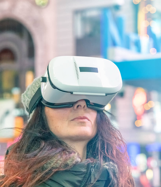 Jeune femme hypnotisée portant des lunettes VR la nuit à Times Square, rayons lumineux venant d'en haut, Manhattan
. - Photo, image