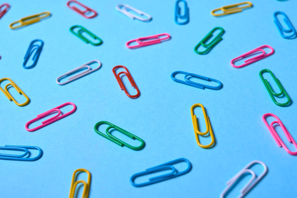 Colorful paper clips on blue background, copy space. Top view. Back to school, college, education concept. White, pink, blue, red, yellow, green paperclips. Abstract background - Фото, изображение
