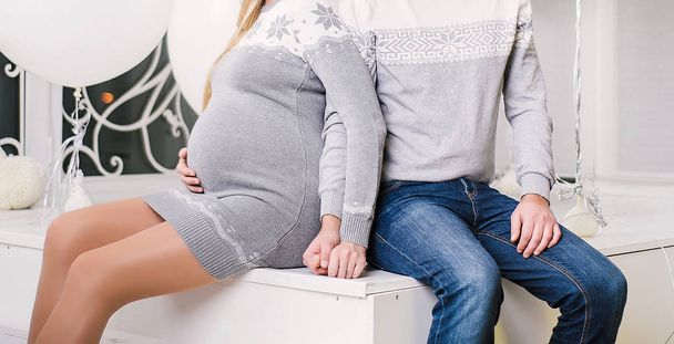 Happy pregnant woman and her husband sitting on stairs, holding hands and touching belly, copy space. Pregnancy and expectation concept - Photo, Image