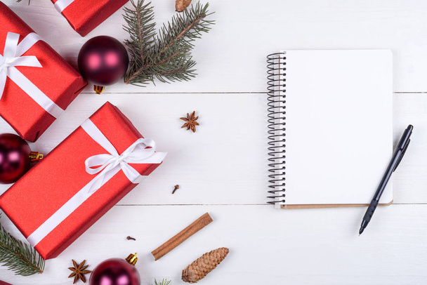 Top view of blank notebook on white wooden background with xmas decorations, copy space. Christmas background with notebook for wish list or to do list, red gift boxes, fir tree branches. Flat lay - Zdjęcie, obraz