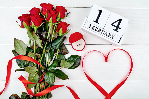 Valentines Day background with bouquet of red roses, diamond ring, ribbon shaped as heart and february 14 wooden calendar, copy space. Greeting card mockup. Love concept. Top view, flat lay - Foto, immagini