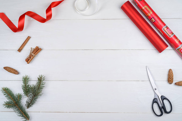 Rouleaux de papier d'emballage de Noël rouge avec ruban, branches de sapin, cônes, cannelle et ciseaux sur fond blanc en bois, espace de copie. Fond de Noël avec décorations, plan plat, vue sur le dessus
  - Photo, image