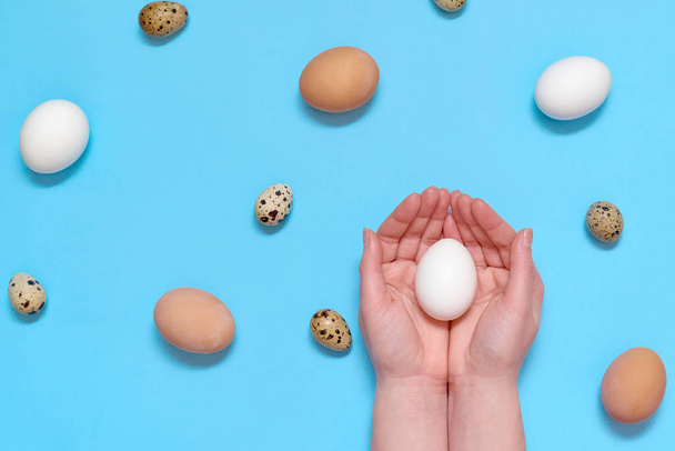 Woman holding white egg in hands with eggs on blue background, copy space. Healthy food concept. Top view, flat lay. Easter eggs. Happy Easter concept - Valokuva, kuva