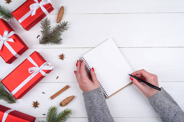 Widok z góry Christmas background z puste pusty dziennik i ręce dziewczyny z piórem, pisanie cele na białym tle drewnianych, wolnego miejsca. Widok płaski świeckich, top - Zdjęcie, obraz