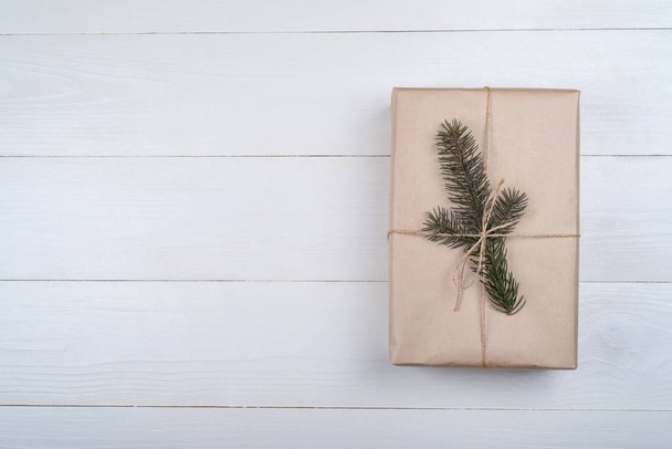 Christmas background with one gift box wrapped in kraft paper with fir tree branch on white wooden background, free space. Holiday greeting card, copy space. Flat lay, top view  - Foto, Bild