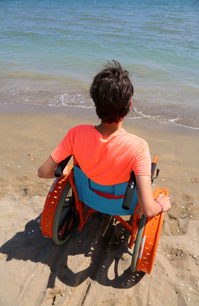 jovem rapaz deficiente em uma cadeira de rodas especial à beira-mar
 - Foto, Imagem
