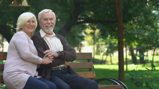 Old couple sitting on bench and happily watching their grandchildren having fun - Кадри, відео