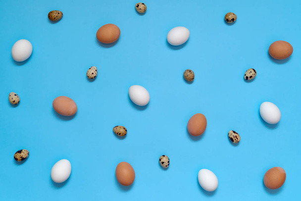 Hen white and brown eggs and quail eggs on blue background, copy space. Healthy food concept. Top view, flat lay. Easter eggs. Happy Easter concept - Photo, image