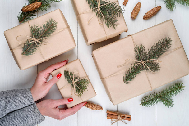 Christmas gift wrapping background, copy space. Female hands holding christmas present box wrapped in kraft, top view. Winter holidays concept, flat lay. Woman with red manicure packing Christmas gift - Foto, Imagem