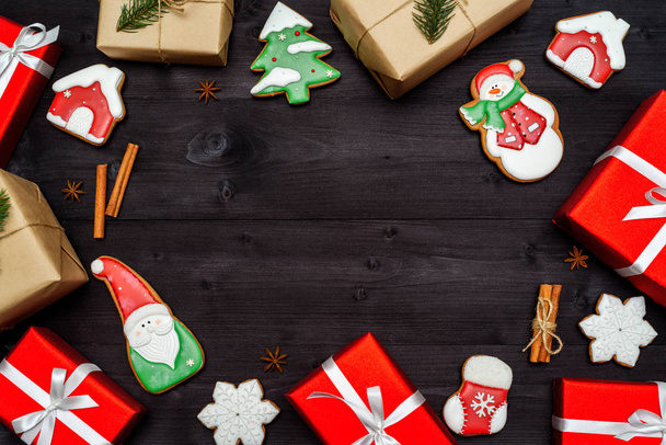 Christmas gingerbread cookies, gift boxes wrapped in craft paper with fir tree branch and red presents on dark wooden background, copy space. Top view, flat lay - Φωτογραφία, εικόνα