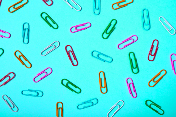 Colorful paper clips on turquoise background, copy space. Top view, flat lay. Back to school, college, education concept. White, pink, blue, red, orange, green paperclips. Abstract background - Photo, image