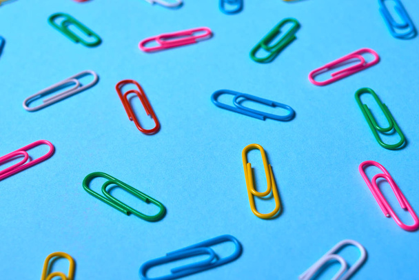 Colorful paper clips on blue background, copy space. Top view. Back to school, college, education concept. White, pink, blue, red, yellow, green paperclips. Abstract background - Φωτογραφία, εικόνα