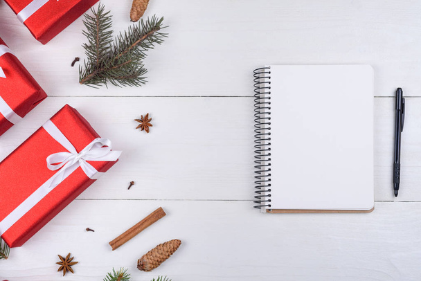 Top view of blank notebook on white wooden background with xmas decorations, copy space. Christmas background with notebook for wish list or to do list, red gift boxes, fir tree branches. Flat lay - Fotó, kép