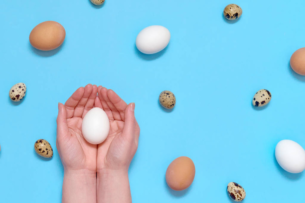 Woman holding white egg in hands with eggs on blue background, copy space. Healthy food concept. Top view, flat lay. Easter eggs. Happy Easter concept - Foto, Imagen