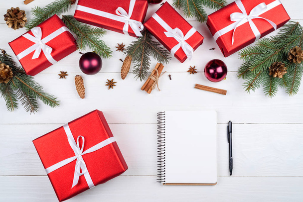 Blank notebook for New year goals (or to do list), red gift boxes, fir tree branches, cones, cinnamon and baubles on white desk, copy space. Christmas background. Top view, flat lay  - Zdjęcie, obraz