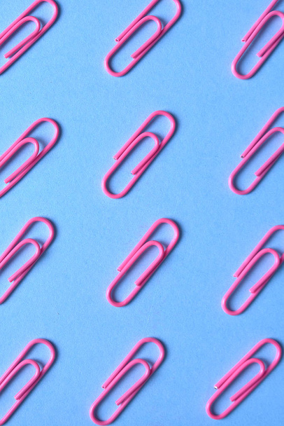 Pink paper clips isolated on blue background, close up, copy space. Top view, flat lay. Back to school, college, education concept - Фото, изображение