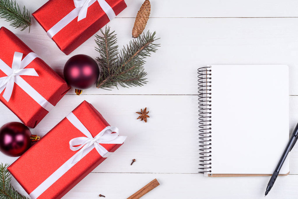 Top view of blank notebook on white wooden background with xmas decorations, copy space. Christmas background with notebook for wish list or to do list, red gift boxes, fir tree branches. Flat lay - Φωτογραφία, εικόνα