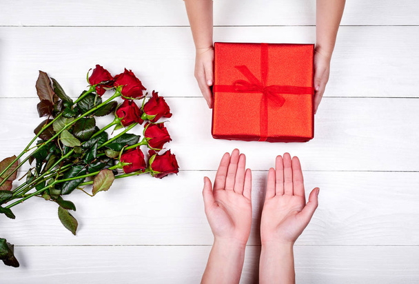 Son giving gift box and flowers to mum, top view. Holidays, present, childhood concept. Close up of child and mother hands with gift box on white background. Mothers day, Womens day, March 8, birthday - Photo, image