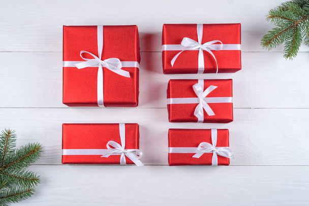 Sfondo natalizio con scatole regalo rosse e rami di abete. Scatole regalo di Natale rosse su sfondo bianco in legno. Biglietto di auguri. Posa piatta, vista dall'alto
  - Foto, immagini