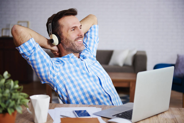 Satisfied man resting and listening to music in his office - 写真・画像