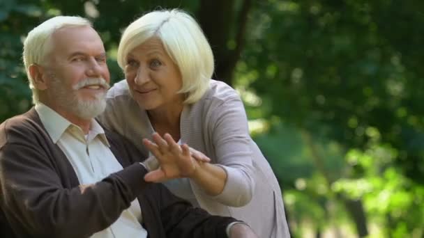 Starsza para przytulanie i szczęśliwie oglądania na swoich wnuków, grając w parku - Materiał filmowy, wideo
