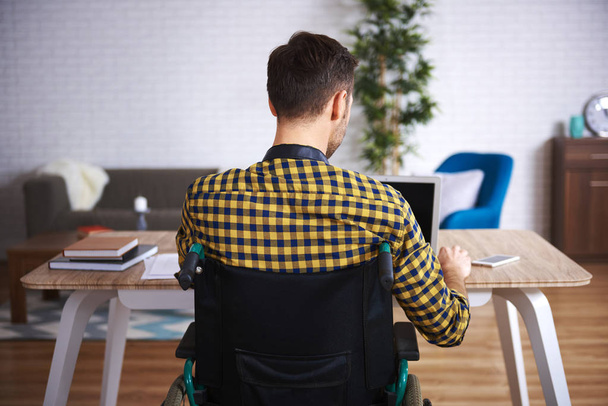 Vue arrière de l'homme handicapé utilisant un ordinateur portable
 - Photo, image