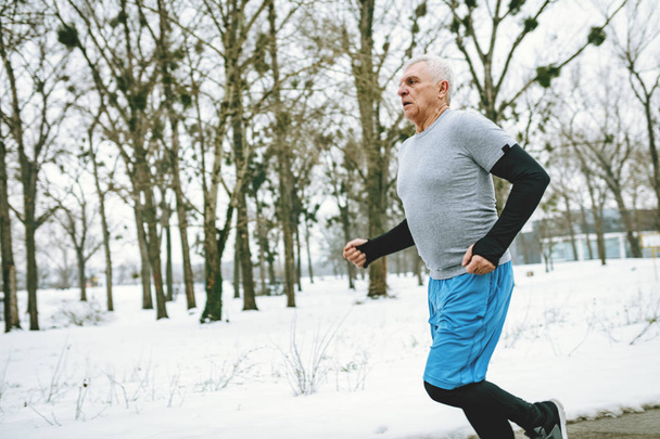 Aktiivinen vanhempi mies juoksemassa puistossa talvikoulutuksen aikana
  - Valokuva, kuva