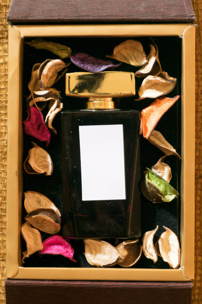 Perfume glass bottle inside golden gift box and colorful leaves with white blank label - Photo, Image