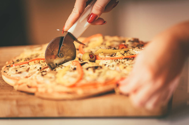 Vista cercana de la mujer cortando pizza fresca casera
 - Foto, Imagen