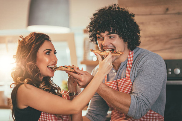 Jeune homme et jeune femme se nourrissant mutuellement de morceaux de pizza
 - Photo, image