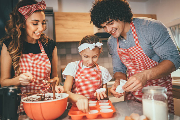 Giovani genitori con figlia che preparano la pasta per muffin in cucina
 - Foto, immagini