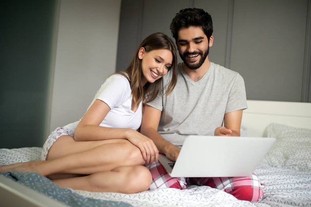 Young couple relaxing on bed with laptop. Love, happiness, technology, people and fun concept. - Zdjęcie, obraz