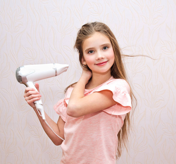 Cute smiling little girl child drying her long hair with hair dryer isolated - Foto, imagen