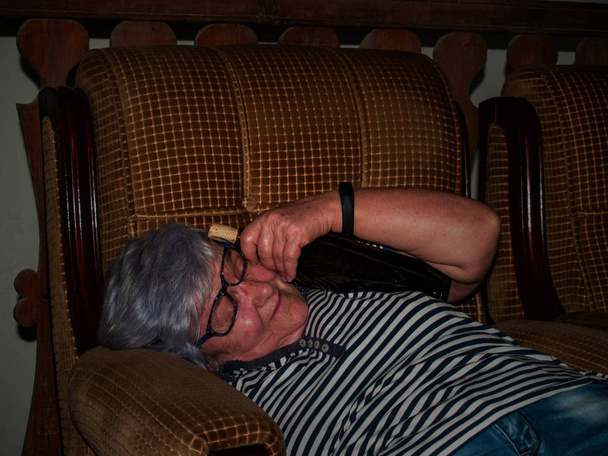 Juoppo vanhempi nainen viinipullo kädessään, tajuton, makaa sohvalla
 - Valokuva, kuva