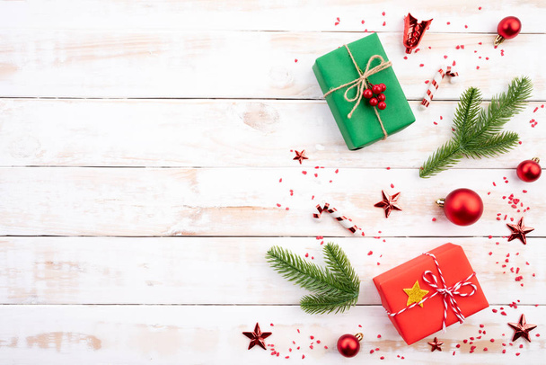 Vánoční pozadí konceptu. Pohled Vánoce, zelené a červené krabičky s smrkových větví, šišky, červené bobule shora a zvonek na bílém pozadí dřevěná. - Fotografie, Obrázek