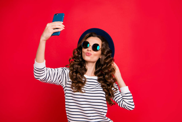 Portrait d'une jolie jolie dame aux cheveux ondulés portant un chapeau de soleil à rayures faisant un selfie romantique isolé sur un fond rouge brillant vif
 - Photo, image