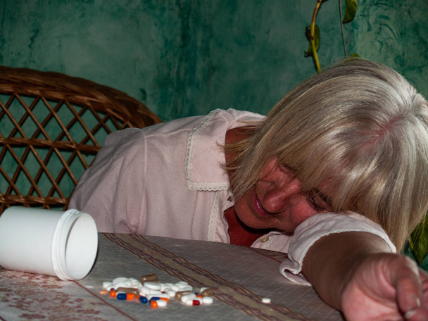 Una donna anziana con un sacco di pillole in mano di diversi colori e dimensioni, sdraiata su un tavolo
 - Foto, immagini