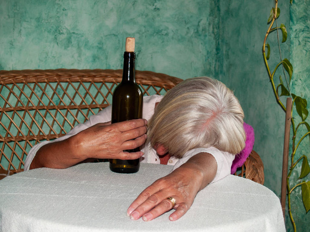 Una mujer mayor con una botella de vino y un gran número de pastillas en la mano de diferentes colores y tamaños, acostada en una mesa
 - Foto, imagen