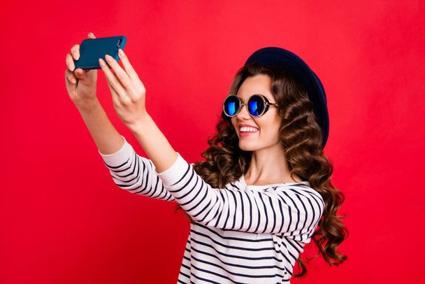 Portrait of nice sweet lovely attractive adorable cheerful positive wavy-haired lady wearing striped pullover sunhat taking making cool trendy selfie isolated over bright vivid shine red background - 写真・画像