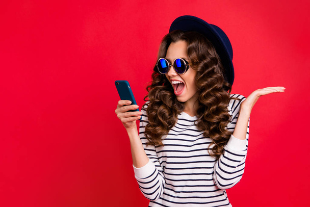 Portrait of nice funny lovely attractive cheerful positive wavy-haired lady in striped pullover eyeglasses eyewear sunhat reading sms opened mouth isolated over bright vivid shine red background - Foto, Bild