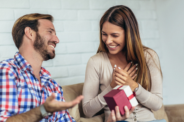 Lächelnder junger Mann überrascht fröhliche Frau mit Geschenkbox zu Hause - Foto, Bild