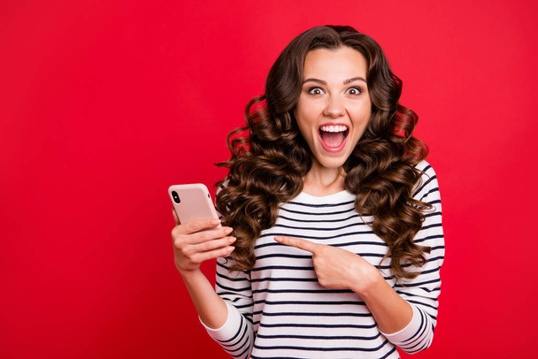 Portrait of nice lovely crazy funny attractive amazed wondered stunned wavy-haired lady wearing striped pullover pointing at screen sms notification great isolated on bright vivid shine red background - Fotoğraf, Görsel