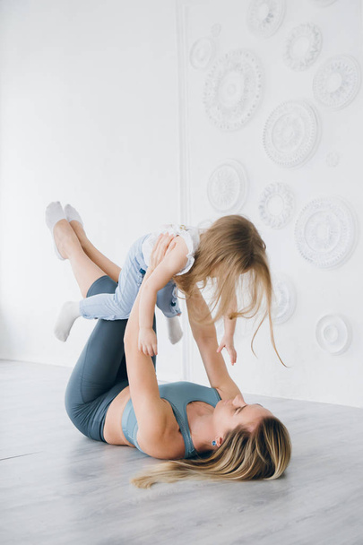 Young sporty mother and baby girl do exercises together in the gym. Parent and child healthy development, fitness and relaxation. Healthy lifestyle concept photo. Toning. - Фото, изображение