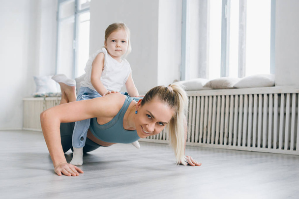 Young sporty mother and baby girl do exercises together in the gym. Parent and child healthy development, fitness and relaxation. Healthy lifestyle concept photo. Toning. - Foto, immagini