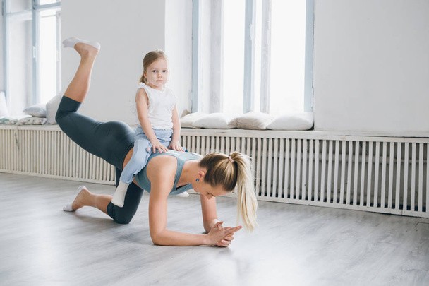 Young sporty mother and baby girl do exercises together in the gym. Parent and child healthy development, fitness and relaxation. Healthy lifestyle concept photo. Toning. - Foto, immagini