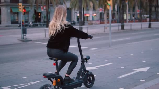 Mujer rubia bonita conduciendo bicicleta eléctrica en la ciudad
 - Metraje, vídeo