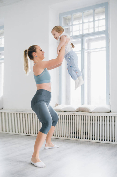 Young sporty mother and baby girl do exercises together in the gym. Parent and child healthy development, fitness and relaxation. Healthy lifestyle concept photo. Toning. - Foto, Imagen