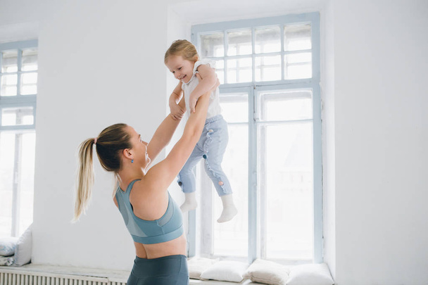 Young sporty mother and baby girl do exercises together in the gym. Parent and child healthy development, fitness and relaxation. Healthy lifestyle concept photo. Toning. - Fotoğraf, Görsel