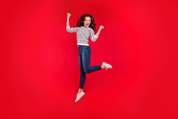 Full length size body portrait of jumping high beautiful pretty charming she her girl raised hands wearing white striped casual sweater and jeans on red vivid bright background - Фото, зображення